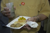 Kellner auf einer Veranstaltung serviert Raclettegericht im Mehrzweckteller und Getränk aus dem Plastikglas.