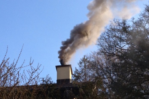 Aus einem Kamin eines Wohnhauses steigt scharzer Rauch.