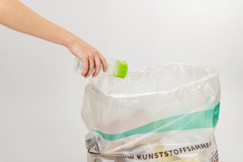 Eine Plastikflasche wird in einem Sammelsack entsorgt.